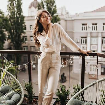 Žena na balkóně v bílé košili a kalhotách