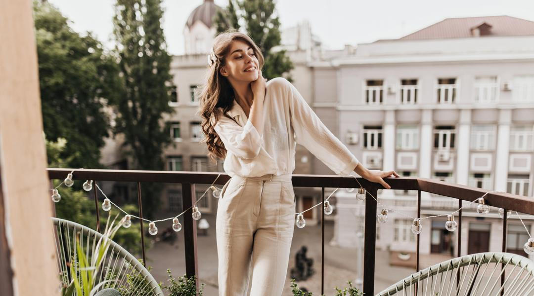 Žena na balkóně v bílé košili a kalhotách