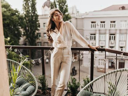 Žena na balkóně v bílé košili a kalhotách