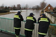Hasiči na mostě sledují naplněné koryto říčky Mrliny