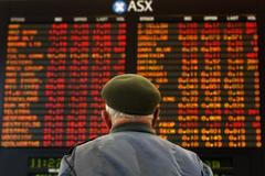 Muž sleduje panel s vývojem akcií na burze v australském Melbourne