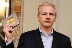 Julian Assange drží v ruce dokumenty k WikiLeaks