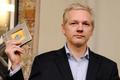Julian Assange drží v ruce dokumenty k WikiLeaks
