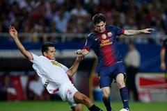 Fotbalista Barcelony Lionel Messi prochází přes Emira Spahiče v utkání španělské La Ligy 2012/13 se Sevillou.