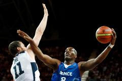 Francouzský basketbalista Ali Traore se snaží smečovat přes Američana Kevina Loveho v utkání základní skupiny A mezi USA a Francií na OH 2012 v Londýně.