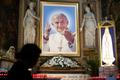 A woman prays in front of a painting depicting Pope John Paul II in a church in downtown Rome