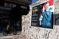 Man on a motorcycle rides past a poster depicting Syria's President Assad on a wall in the pro-government al-Zahraa neighbourhood in Homs