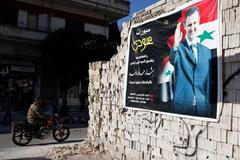 Man on a motorcycle rides past a poster depicting Syria's President Assad on a wall in the pro-government al-Zahraa neighbourhood in Homs
