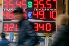 People pass by a board displaying exchange currency rates in Moscow