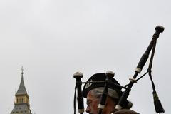 A street performer plays the Scottish bagpipes dressed in traditional Scottish attire on Westminster Bridge in London