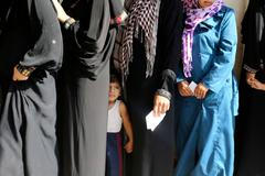 A homeless Palestinian boy stands in line with his mother as they wait to receive aid at a United Nations-run school where they are taking refuge in Khan Younis