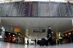 Pilots pass flight schedule board announcing cancelled flights by German air carrier Lufthansa at Munich's airport