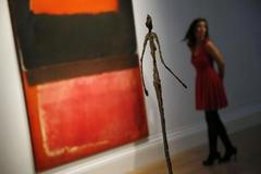 Staff member poses in a gallery near "No. 21 (Red, Brown, Black and Orange)" by Rothko and "Chariot" by Giacometti at Sotheby's auction house in London