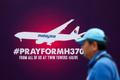 A tourist walks past a signboard saying "Pray for MH370" in front of the Kuala Lumpur City Center