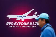 A tourist walks past a signboard saying "Pray for MH370" in front of the Kuala Lumpur City Center