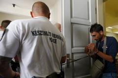 Policista odvádí jednoho ze zadržených pašeráků, podezřelých z podílu na smrti 71 uprchlíků v dodávce.