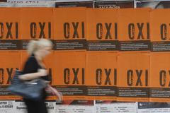 A woman makes her way past posters that show the word 'No' in Greek in Athens