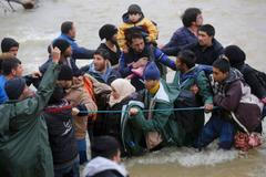 Běženci se brodí řekou, aby se dostali přes uzavřenou hranici mezi Řeckem a Makedonií.