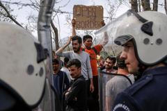 Migrants and refugees stand in front of Greek policeman after they tried to open the border fence at a makeshift camp at the Greek-Macedonian border near the village of Idomeni
