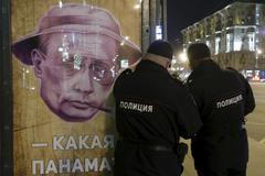 Policisté u plakátu s Putinem na autobusové zastávce v Moskvě.