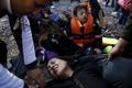 An Afghan migrant woman collapses in exhaustion soon after arriving on an overcrowded raft at a beach on the Greek island of Lesbos