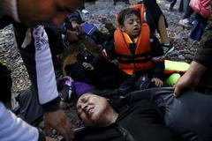 An Afghan migrant woman collapses in exhaustion soon after arriving on an overcrowded raft at a beach on the Greek island of Lesbos