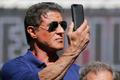 Cast member Sylvester Stallone holds a mobile phone as he poses on a tank arriving on the Croisette to promote the film "The Expendables 3" during the 67th Cannes Film Festival in Cannes