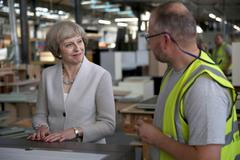 Theresa Mayová hovoří s truhlářem v londýnské továrně.
