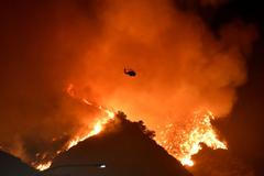 A firefighting helicopter flies over the Getty Fire as it burns in the hills west of the 405 freeway in the hills of West Los Angeles, California