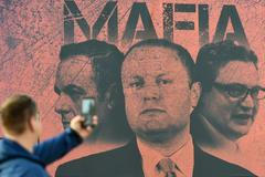 Muž fotografuje plakát, zobrazující maltského premiéra Josepha Muscata a jeho dva ministry jako mafii.