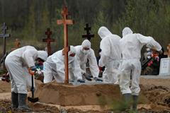 Hrobníci ukládají do země rakev s ostatky jedné z oběti nemoci covid-19 v Petrohradu.