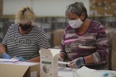 Pracovníci České pošty balí do obálek pět roušek a respirátor pro lidi starší 60 let