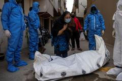 Lidé v ochranných oblecích odnášejí jednu z obětí nemoci covid-19 v Dillí.