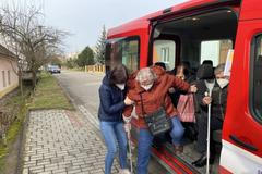 Hasiči vykládají z dodávky jednu ze seniorek, kterou odvezli na očkování proti covidu.