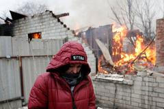 Ukrajinka stojí vedle svého domu, který byl poškozen ostřelováním v Doněcku a zachvátil ho požár.