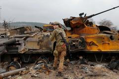 Ukrajinský voják před zbytky ruské techniky nedaleko Kyjeva.