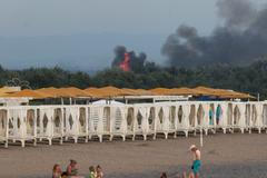 Skupina Rusů je na krymské pláži, zatímco v pozadí hoří letecká základna Saky.