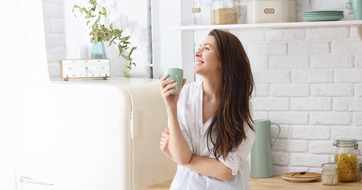 Young happy woman drinking coffee on the kitchen in the morning
