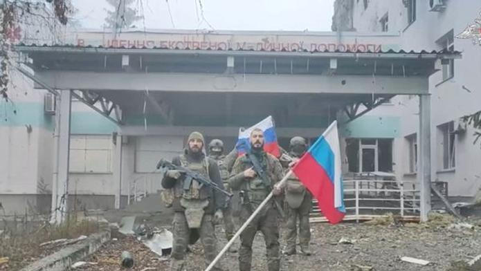 Ruští vojáci drží ruské vlajky před nemocnicí v Kupjansku v Charkovské oblasti na Ukrajině. Snímek pochází z videa zveřejněného 21. listopadu 2025.