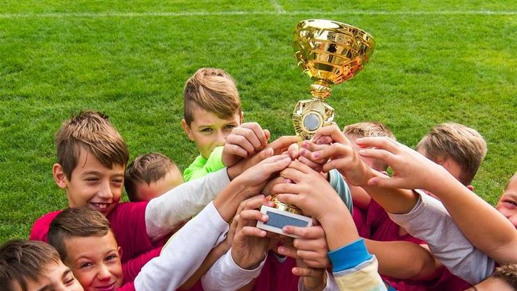 Kids soccer football - young children players celebrating with a trophy after match on soccer field