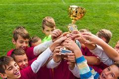 Kids soccer football - young children players celebrating with a trophy after match on soccer field