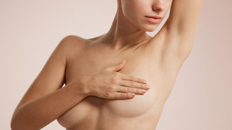 ["Closeup cropped portrait young woman with breast pain touching chest colored isolated on background"]