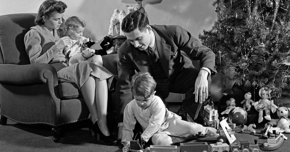 1930s 1940s FAMILY AROUND CHRISTMAS TREE BOY PLAYING WITH TRAIN DAD HELPING MOM AND GIRL IN CHAIR