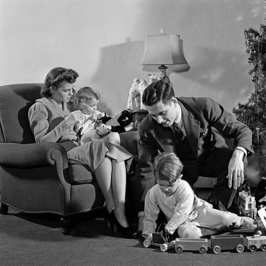 1930s 1940s FAMILY AROUND CHRISTMAS TREE BOY PLAYING WITH TRAIN DAD HELPING MOM AND GIRL IN CHAIR