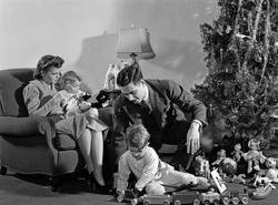 1930s 1940s FAMILY AROUND CHRISTMAS TREE BOY PLAYING WITH TRAIN DAD HELPING MOM AND GIRL IN CHAIR