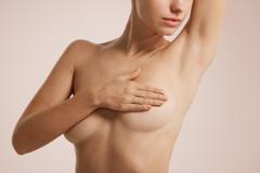 ["Closeup cropped portrait young woman with breast pain touching chest colored isolated on background"]
