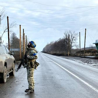Ukrainian serviceman checks the sky for Russian combat drones as he stands at a road near the frontline city of Kupiansk