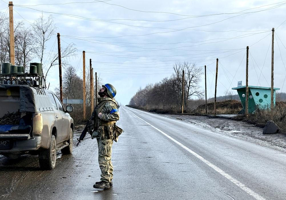 Ukrainian serviceman checks the sky for Russian combat drones as he stands at a road near the frontline city of Kupiansk