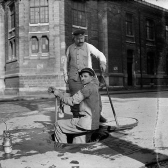 Čištění kanalizací zahrnuje odstraňování usazenin a nečistot z kanalizačních sítí pomocí speciálních nástrojů a techniky. Pracovníci čelí riziku kontaktu s nebezpečnými chemikáliemi a biologickým odpadem. Práce se odehrává v uzavřených prostorách s minimem ventilace a vyžaduje ochranné pomůcky. Na snímku jsou dělníci kanalizace při práci v ulicích Paříže, 1943.