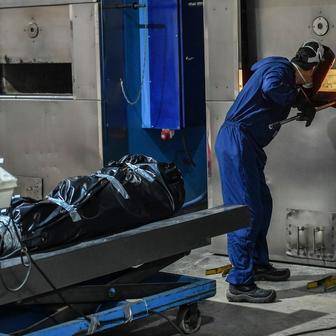 Operátoři krematorií manipulují s mrtvými těly při jejich spalování. Pracovník krematoria obsluhuje pec v Campos de Paz v Medellínu, Kolumbie, 19. června 2021. Na snímku tělo oběti pandemie COVID-19.